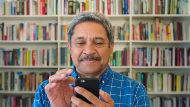 Older Male Bookstore Owner Using Phone Senior Latino Man Browsing — Stockvideo