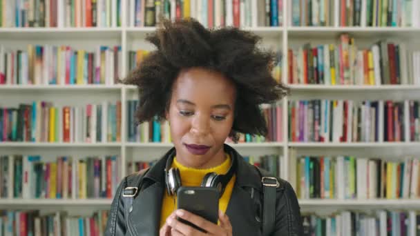 Stijlvolle Afro Vrouw Typt Haar Telefoon Een Boekwinkel Bibliotheek Funky — Stockvideo