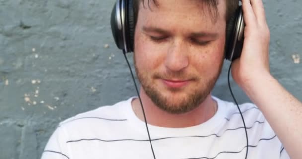 Видеозапись Красивого Молодого Человека Слушающего Музыку Наушниках Стоящего Кирпичной Стены — стоковое видео