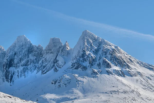 A cold mountain peak covered in snow during winter with a blue sky background. Beautiful landscape of a snowy summit with freezing weather conditions in the morning outdoors in nature.