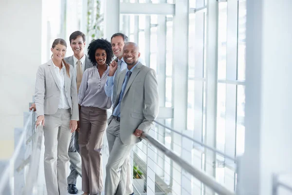 Dynamic group of colleagues stand in their workplace while looking at you - Copyspace.