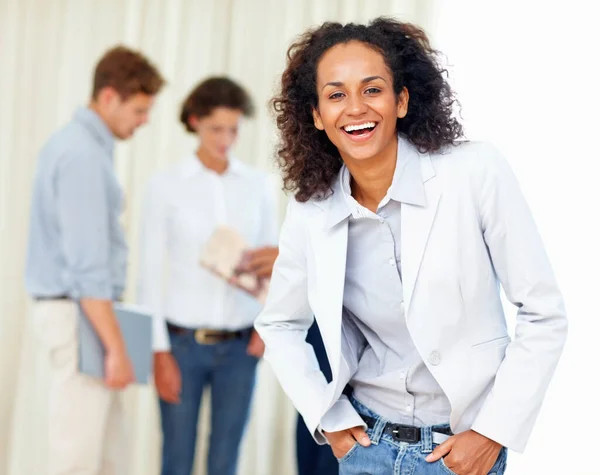 Beautiful business woman with hands in pockets and colleagues discussing in background.