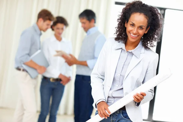 Young business woman holding blueprint with colleagues discussing in background.