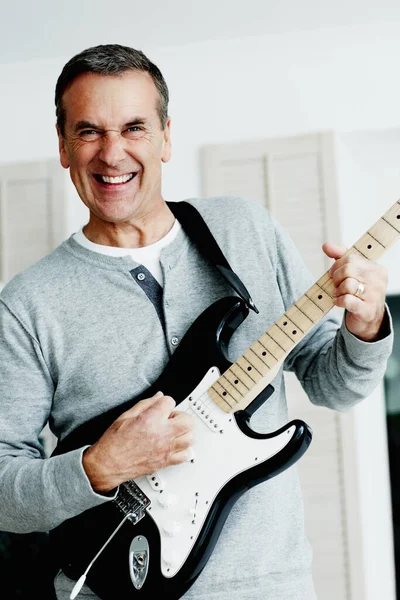 Portrait of a cheerful mature man playing an acoustic guitar.