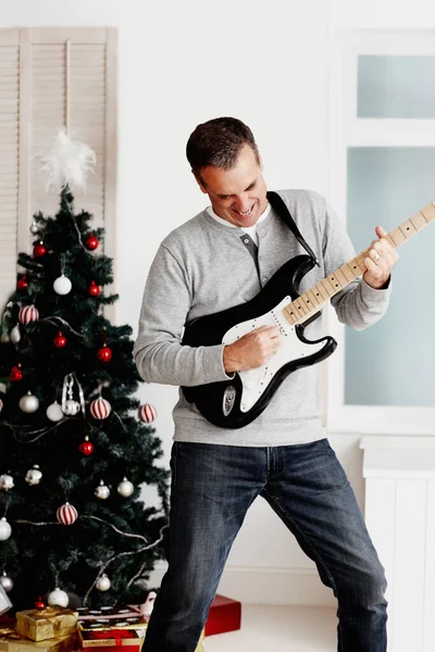 Portrait of a joyful mature man playing guitar during Christmas.