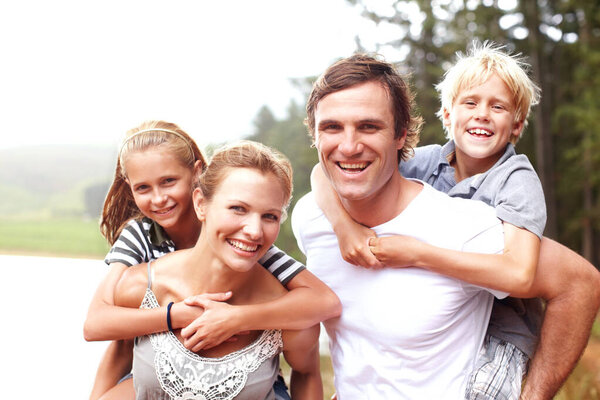 Happy young parents piggybacking their children and smiling while outdoors - portrait.