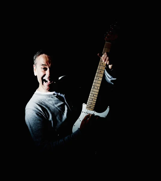 Portrait of a joyful mature man playing an acoustic guitar against black background.