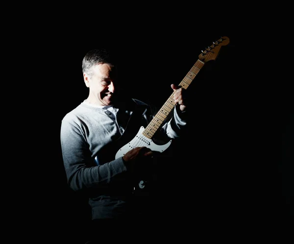 Portrait of a cheerful mature man playing guitar against black background.