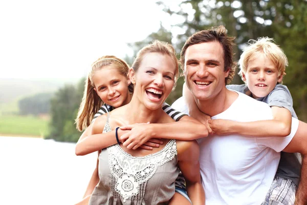 Laughing Young Parents Piggybacking Children While Outdoors Portrait Stockfoto