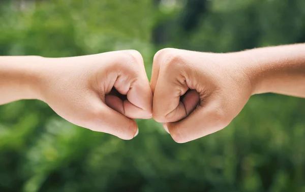 Closeup of a fist bump outside in nature. Two diverse peoples hands greeting. Fist bump in nature.