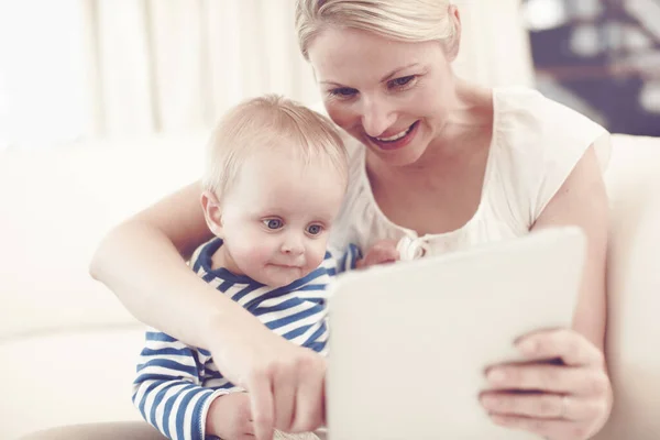 An attractive young mother showing her curious baby a touchscreen tablet.