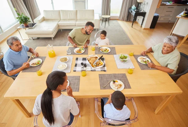 Overhead view of a mixed race family sitting at a table having lunch in the lounge at home. Hispanic grandparents having a meal with their kids and grandkids at home.