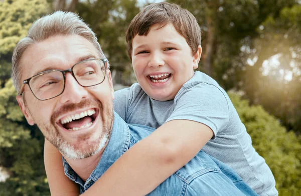 Happy caucasian father carrying playful little son on his back for piggyback ride in garden or backyard outside. Smiling parent bonding with adorable child. Kid enjoying relaxing free time with dad.