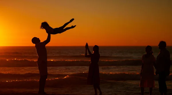 A young family silhouetted on the beach while playing together. Cheerful family with one child, two parents and daughter having fun during sunset at the beach.
