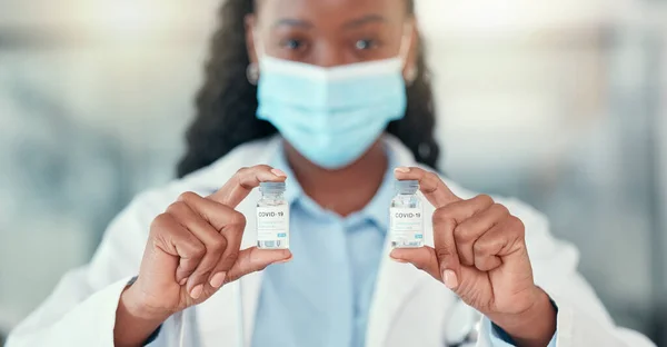 Medical doctor holding bottles of the covid cure. Ready to save the world from covid. African American doctor holding vials of the corona virus antidote.Healthcare professional wearing a mask.