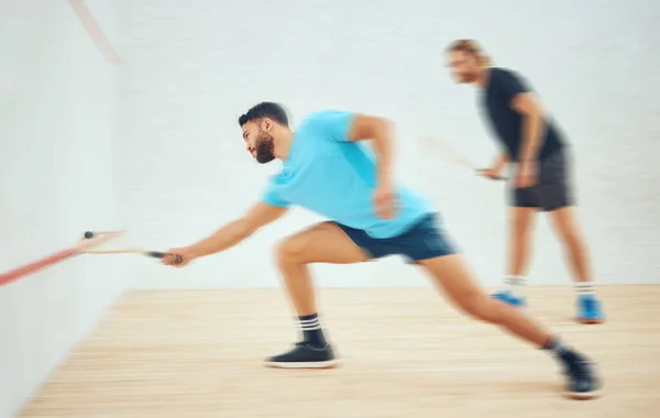Two athletic squash players playing match during competitive court game. Fit active mixed race and caucasian athlete competing during training challenge in sports centre. Full length with motion blur.
