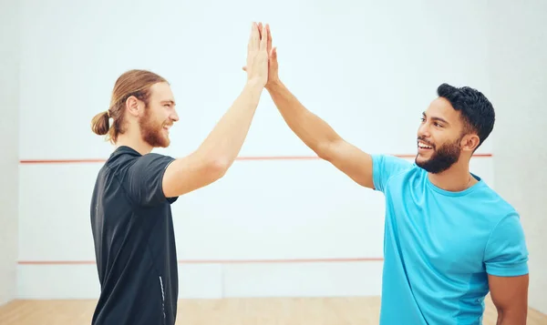 Two athletic squash players giving high five before game on court. Team of fit active caucasian and mixed race male athletes using hand gesture before competing and training together in sports centre.