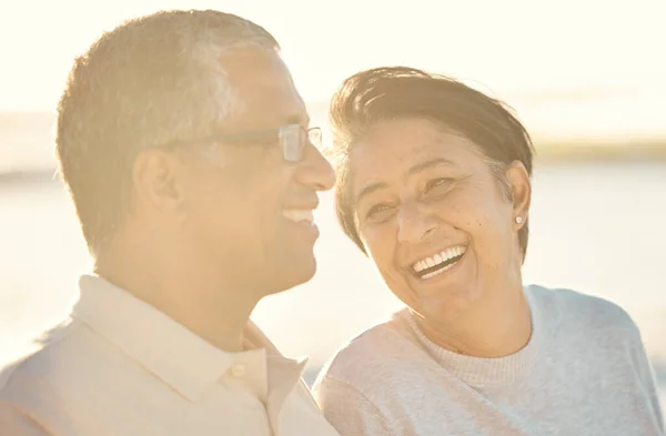 A senior mixed race couple walking together on the beach smiling and laughing on a day out at the beach. Hispanic husband and wife looking happy and showing affection while having a romantic day on