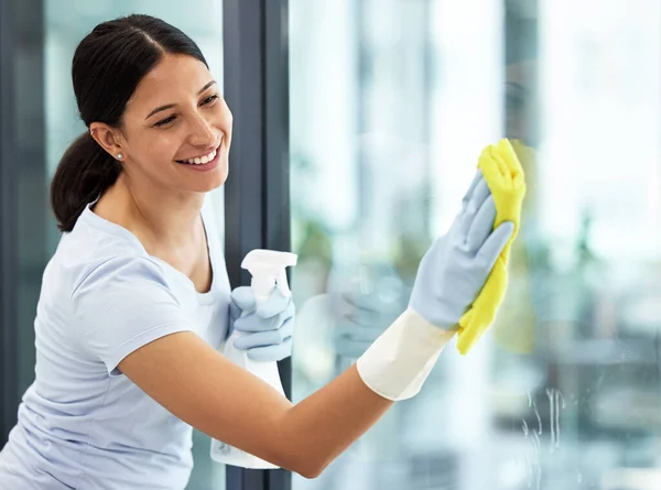 A happy smiling mixed race domestic worker using a cloth on a window. One Hispanic woman enjoying doing chores in her apartment.