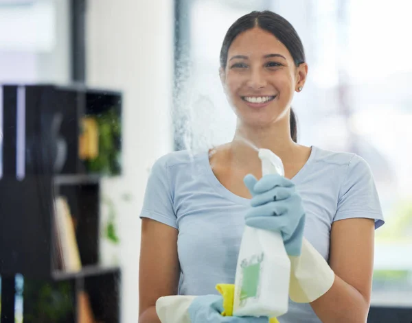 Portrait of a happy mixed race domestic worker using a cloth on a window. One Hispanic woman enjoying doing chores in her apartment.