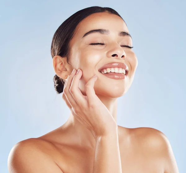 Closeup face beautiful young mixed race woman. Attractive female touching her face in studio isolated against a blue background. A skincare regime to keep your skin soft, smooth, glowing and healthy.