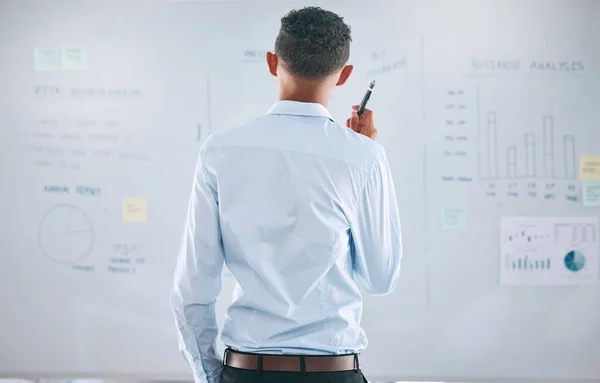 One businessman from behind brainstorming and planning with graphs, stats and analytics on a whiteboard. Mixed race guy thinking of ideas and strategies while doing market research for his startup.