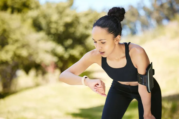 One active young mixed race woman checking digital smartwatch while training outdoors. Hispanic athlete wearing fitness tracker with stopwatch to monitor progress, heart rate and calories burned