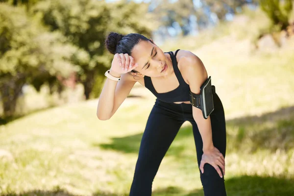 One active young mixed race woman taking a break from exercising outdoors. Hispanic athlete wiping sweat off forehead after a jog or run outside. Woman looking tired after workout.