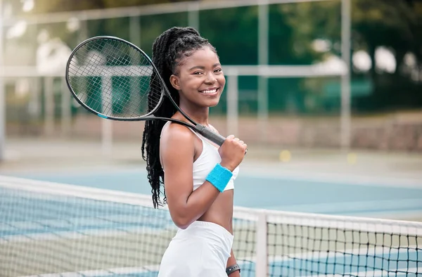 African american woman holding her tennis racket on the court. Young girl ready for a tennis match outside. Smiling woman standing outside at her tennis club ready for a match.