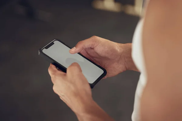 Hands of a bodybuilder using their cellphone in the gym. Closeup on hands of an athlete using their smartphone. Screen of a mobile device being used in the gym. Athlete using online app on phone.