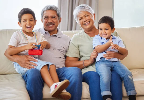 Portrait of smiling grandparents while holding their grandsons on a sofa in the lounge. Senior hispanic man and woman spending time with their grandkids in the lounge at home.