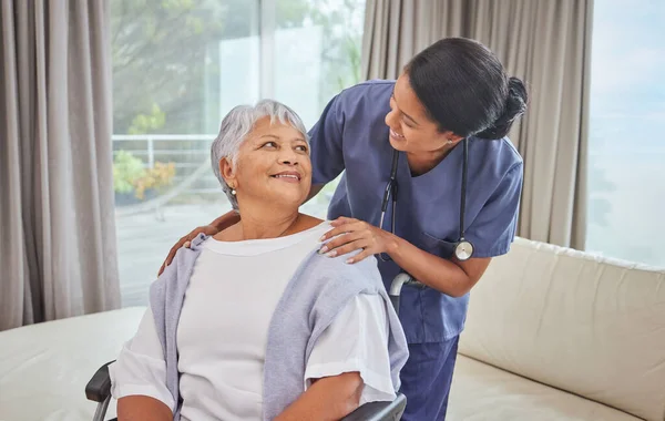 A hispanic senior woman in a wheelchair and her female nurse in the old age home. Mixed race young nurse and her patient in the lounge.