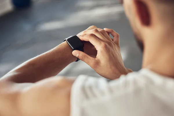 Fit athlete tracking his progress on his watch. Strong athlete using his smartwatch in the gym. Bodybuilder checking the time on his watch. Muscular man timing his workout in the gym.