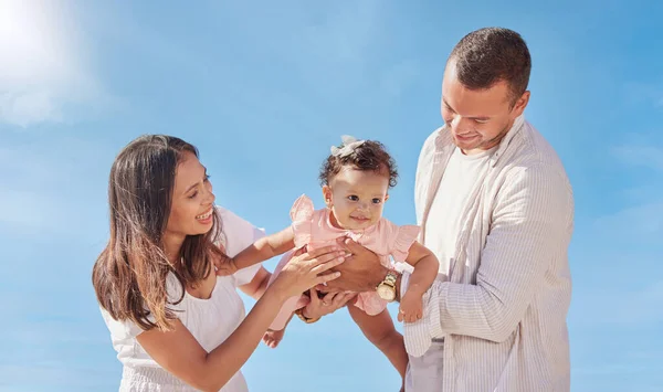 A happy mixed race family of three enjoying fresh air at the beach. Hispanic couple bonding with their newborn daughter playing and having fun.