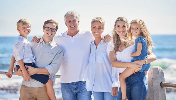Close up of happy caucasian multi-generation family standing together on seaside promenade on a sunny day. Two little children enjoying time at the beach with their parents and grandparents.