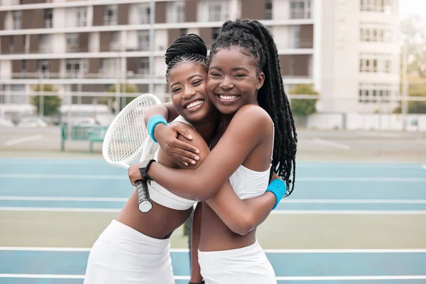 Happy friends hugging after a game of tennis. Cheerful tennis players being affectionate. Professional tennis players embracing after a match. Fit friends bonding on the tennis court.