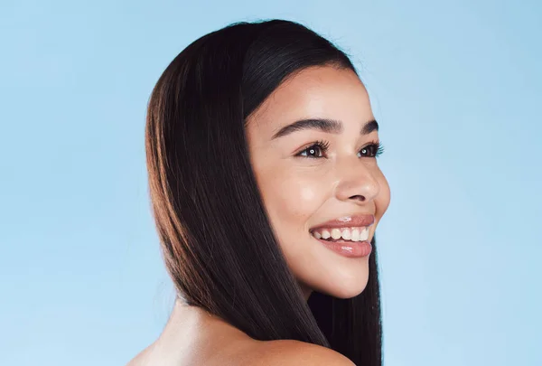 One beautiful young hispanic woman with healthy skin and sleek hair smiling against a blue studio background. Happy mixed race model with flawless complexion and natural beauty.