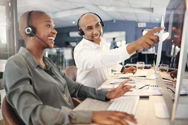 Mixed race male call centre telemarketing agent discussing plans with colleague while working together on computer in an office. Two consultants troubleshooting solution for customer service and sales