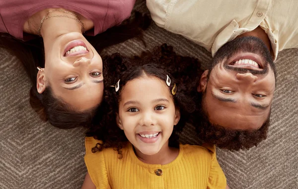 Above portrait of mixed race parents enjoying weekend with daughter in home living room. Smiling hispanic girl hugging mother and father and bonding in lounge. Happy couple lying together with child.