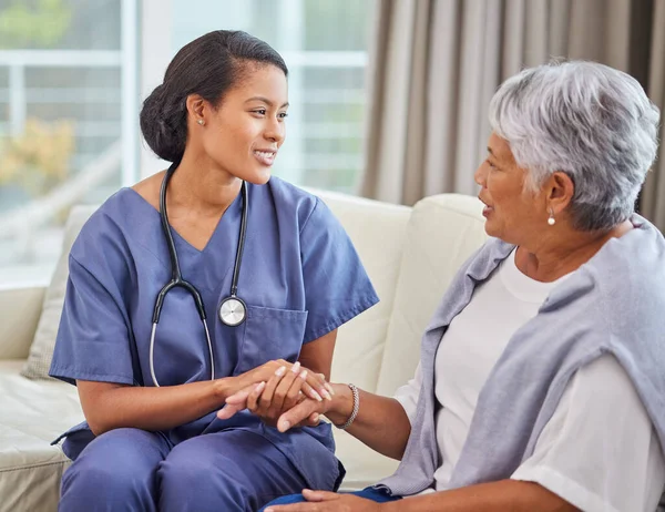 A hispanic senior woman in on a cosy sofa and her female nurse in the old age home. Mixed race young nurse and her patient talking in the lounge.