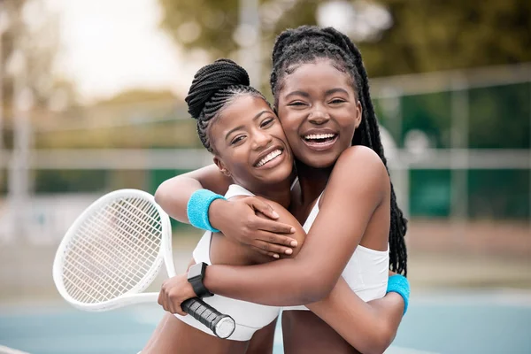 Portrait of two friends hugging after a match. Cheerful young girls embracing after a game of tennis. African american women being affectionate after a tennis match. Happy friends on a tennis court.