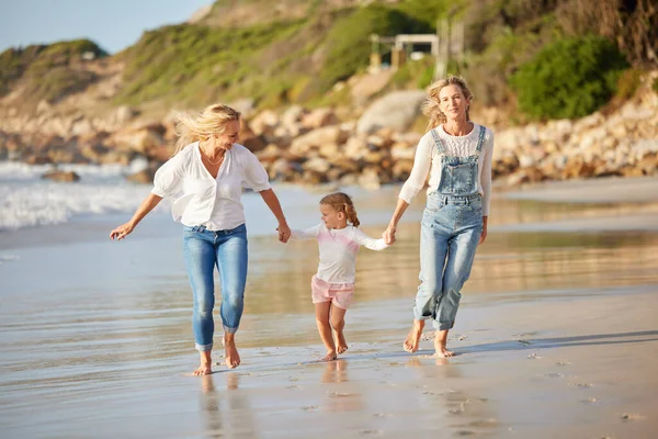 Cute caucasian girl being held outside by her mom and grandmother in the sea at the beach. A young woman and her mom holding cute daughter while walking in the water on the coast at sunset.