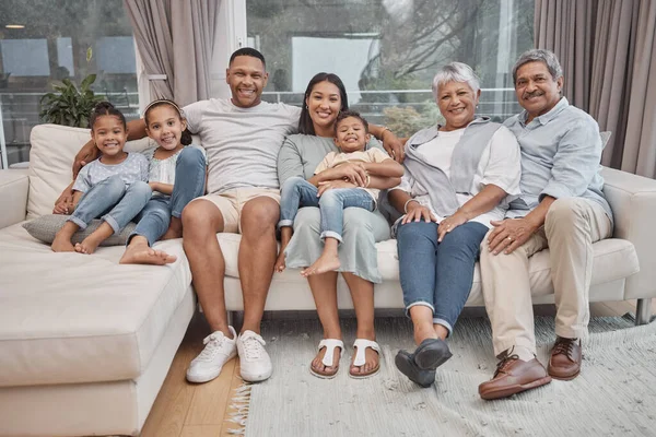 Happy and affectionate young mixed race family of seven sitting on a sofa in the home living room. Married couple with their mother, father, son and daughter in the lounge. Granny and grandpa visit.