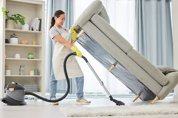 A mixed race domestic worker lifting and cleaning under the sofa. One mixed race female using a vacuum cleaning under a couch to begin spring cleaning.