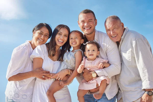 Portrait of smiling mixed race family with little girls standing together on beach. Adorable little kids bonding with mother, father, grandmother and grandfather outside.