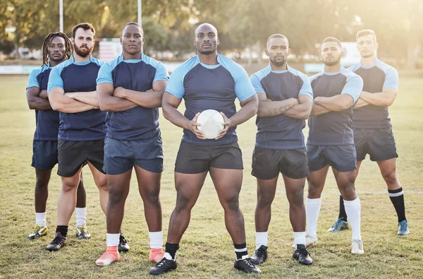 Portrait diverse young rugby players holding a rugby ball while standing with their arms crossed outside on the field. Men looking confident, ready for a match. Athletic sportsmen focused on the game.
