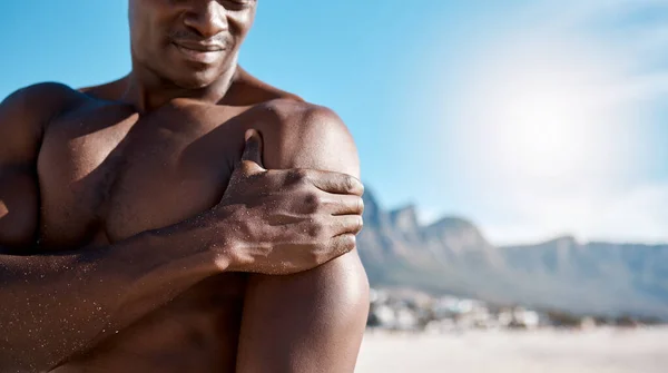 Closeup shot of an african american muscular athletic man holding his shoulder in pain. Black unrecognizable male suffering from arthritis in his arm. Suffering from a hurting, stiff, injured joint.