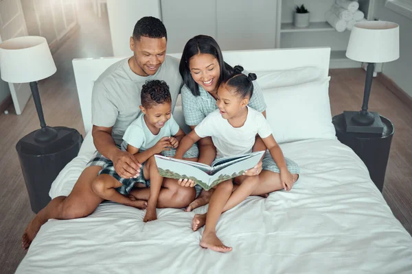 Young mixed race parents mom and dad reading a book to little daughter and son while bonding and spending time together at home in the morning. Two children enjoying fairy tale story while sitting