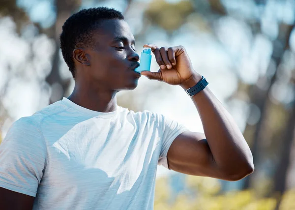 Young african man taking a break from a workout to use his asthma pump. Fit athlete using his asthma inhaler during an asthma attack while exercising outside. Athletic man using a medical treatment.