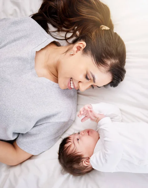 A single mixed race hispanic woman bonding with her newborn baby while talking in bed and having fun. Hispanic woman enjoying being a mother while smiling and talking to her cute little baby.